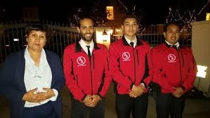 Three A&A Parking Services valet attendants in red uniforms standing at the lit entrance gate of a private residence in the evening