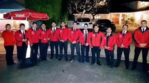 A full A&A Parking Services crew of thirteen valet attendants in red uniforms lined up beside the branded red VALET tent at a private evening event
